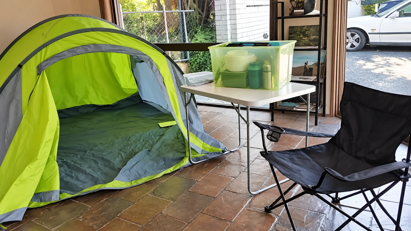 A hire tent pitched beside a camp table, folding chair and a tub of kitchen gear